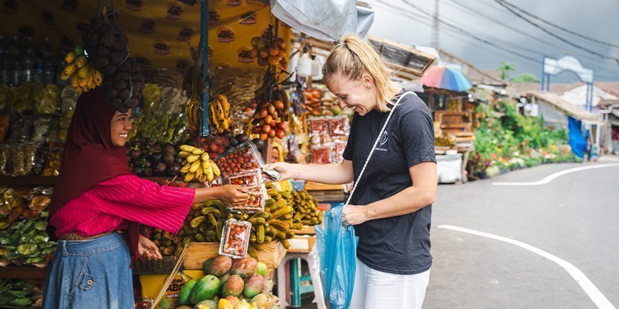 Kvinne i TourCompass-t-skjorte betaler kvinne for varer i en gatebod