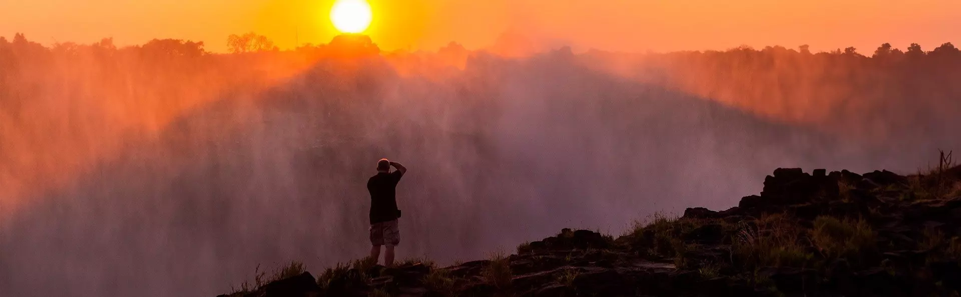 Mann tar bilder av Victoria Falls i skumringen